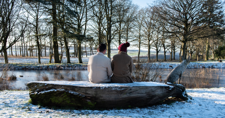 Two people sat on bench in a snow covered grounds at Ushaw Historic House.